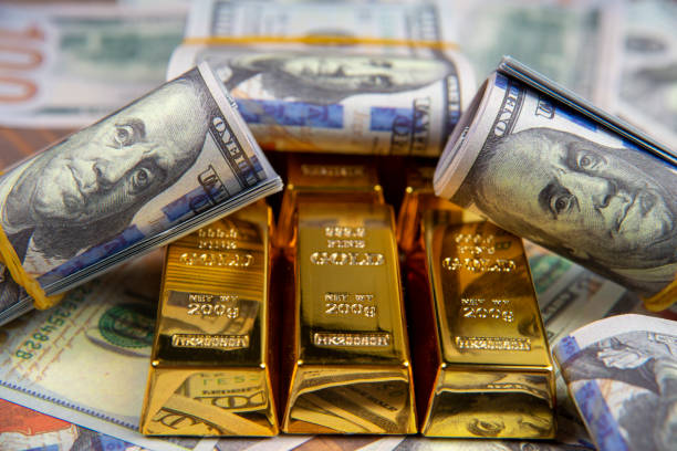 Gold bars and rolls of hundred-dollar bills, symbolizing the relationship between gold prices and the strengthening of the dollar in forex trading.